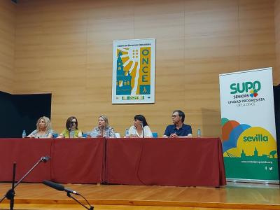 Imagen del escenario donde se desarrolló la Asamblea en la que en el centro se visualiza la mesa con los cinco ponentes quedando a la derecha la enara de SUPO Sevilla