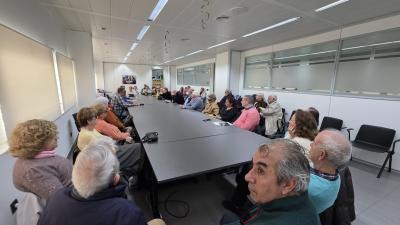 En la imagen se observa el desarrollo de la Asamblea de SUPO en Sevilla en una sala amplia y luminosa, dispuesta para reuniones de trabajo. Los asistentes ocupan los asientos alrededor de una gran mesa rectangular, lo que favorece un ambiente de diálogo y participación directa entre todas las personas presentes. El encuentro reúne a un grupo numeroso de socios y simpatizantes, sentados de forma ordenada, escuchando con atención las intervenciones. Sobre la mesa se aprecian documentos, libretas y algunos dis