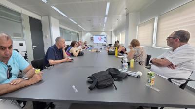 La imagen muestra a un grupo de personas reunidas en una sala del CRE de Sevilla, sentadas alrededor de una mesa y siguiendo en una pantalla una ponencia en formato videoconferencia, en el marco del webinar sobre la “Lucha contra la Soledad No Deseada”. La disposición híbrida, con participantes presenciales y conexión online, refleja un encuentro participativo en el que los asistentes comparten un espacio de atención y trabajo conjunto, acorde con la actividad de reflexión y sensibilización desarrollada por