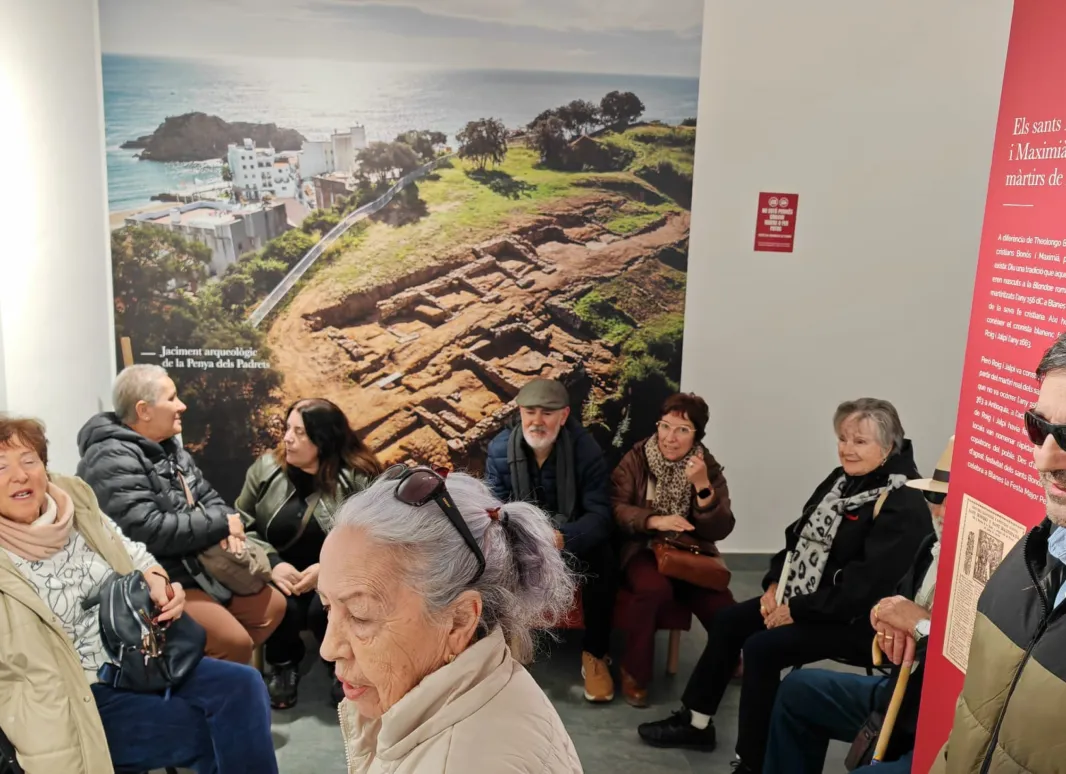 Fotografia que muestra distintos participantes durante la visita a Blandae. Se observa en el fondo una fotografía del antiguo asentamiento romano. 