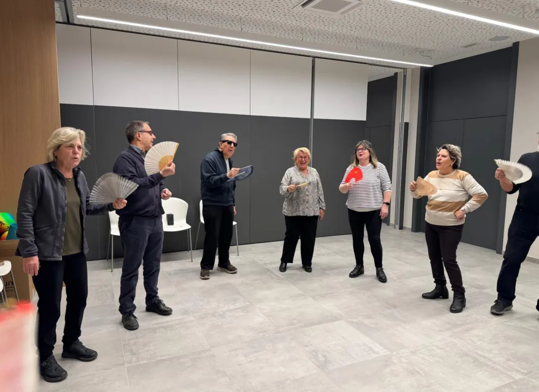 Fotografia en la que aparecen varios participantes, durante el taller de risoterapia en la agencia de la Once en Girona. llevan en la mano un abanico.