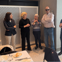 grupo de personas donde una sostiene el micrófono para hablar en una comida 