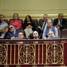 Varias personas asisten sentadas en la tribuna de un salón institucional con barandilla ornamentada.